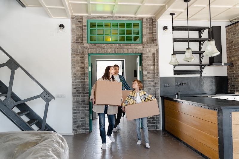 A happy family moving into their new home, carrying moving boxes